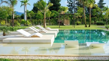 Una piscina con sillas de descanso y una hamaca colgante, rodeada de follaje y palmeras.