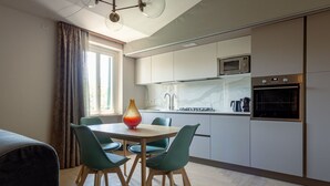 A modern kitchen with white cabinets, a microwave, and an oven. There is a dining table with chairs and a vase on it. - Residence  Tulipe N3004 (Lucca)