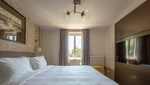A hotel room with a large bed, a TV, a window with curtains, and a radiator.