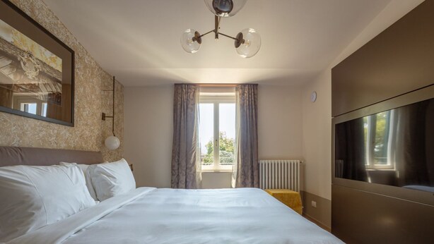 A hotel room with a large bed, a TV, a window with curtains, and a radiator. - Residence  Tulipe N3004 (Lucca)