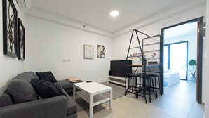 Una sala de estar moderna con un sofá gris, una mesa de centro blanca, un televisor y una zona de bar con taburetes.