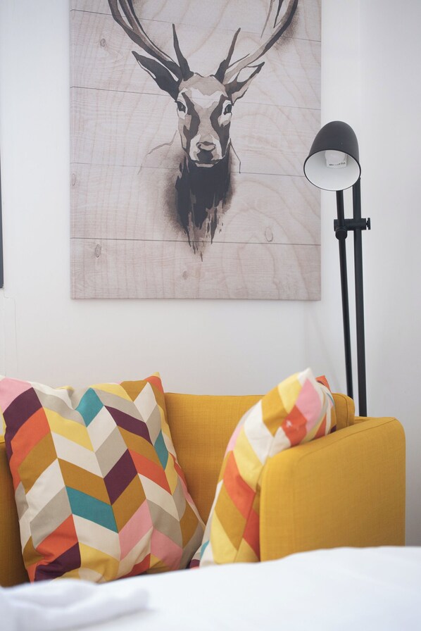 A room with a yellow sofa, colorful chevron-patterned pillows, a wall-mounted deer painting, and a black floor lamp. - PORT CITY HAIFA- Downtown Luxury (Haifa)