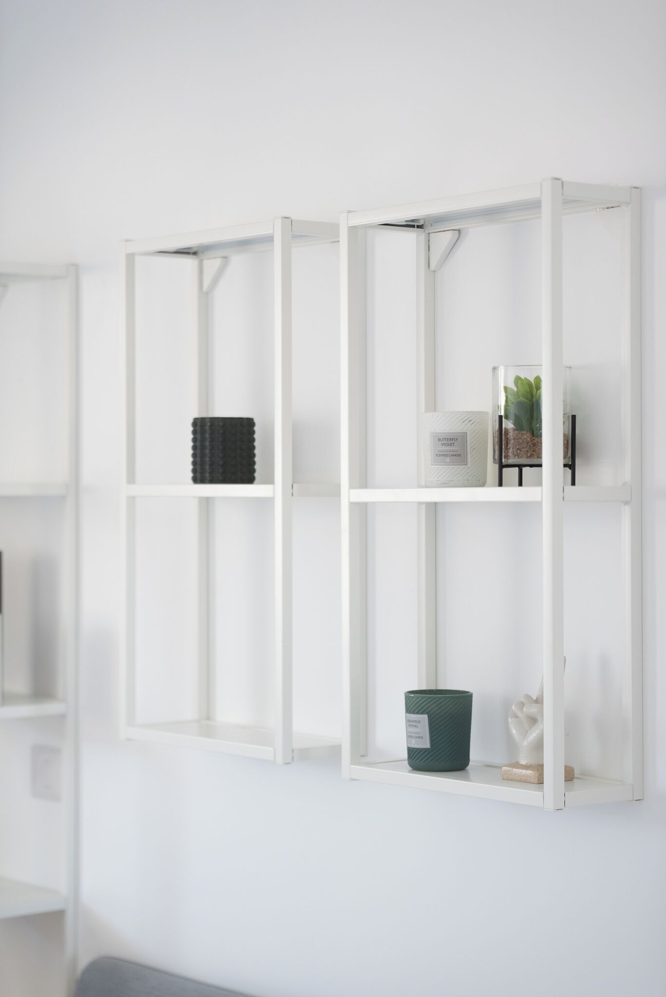 Een wit wandrek met verschillende spullen, waaronder een groene container, een witte container en een kleine plant.