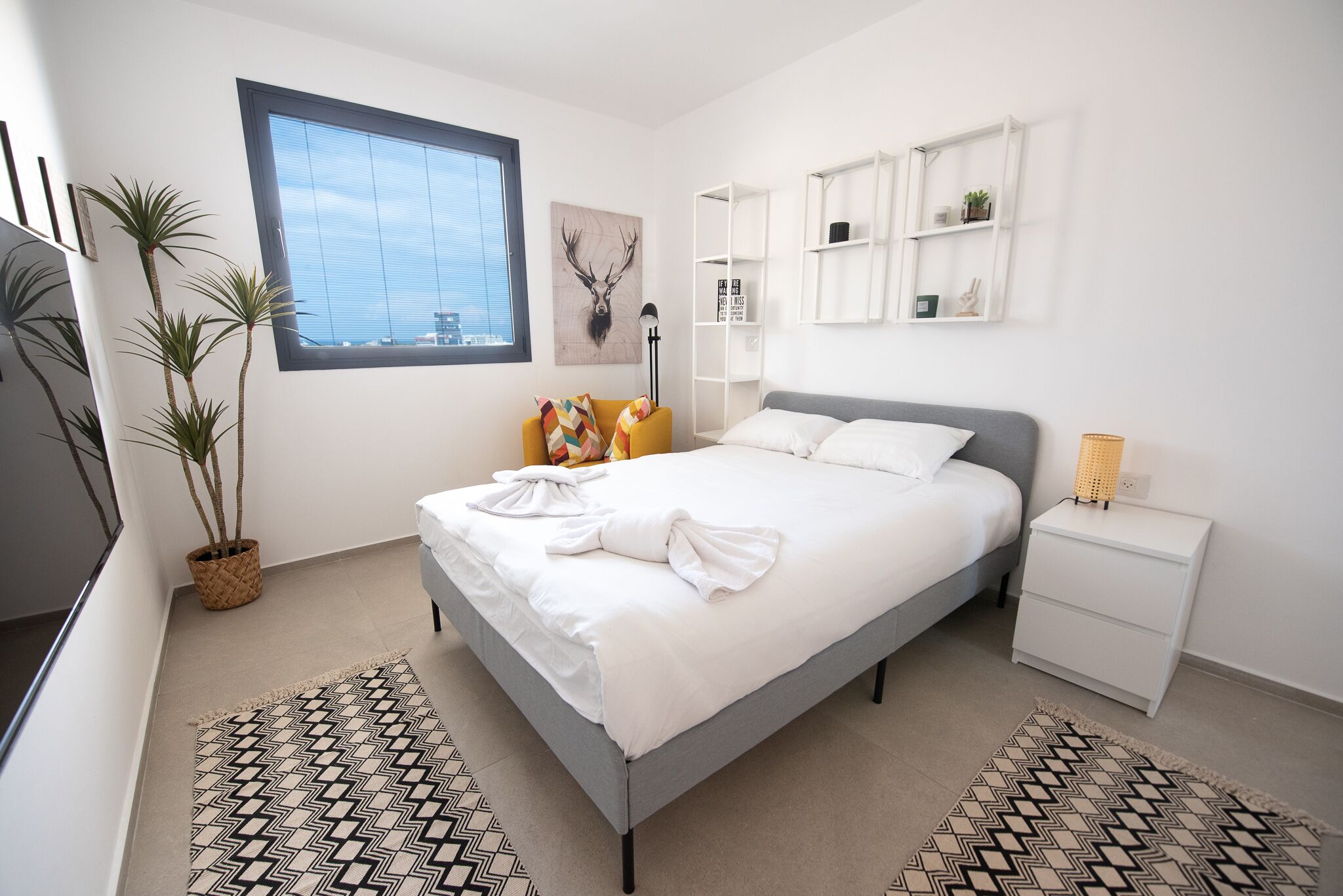 A modern bedroom with a bed, bedside tables, a window, and a wall-mounted shelf.