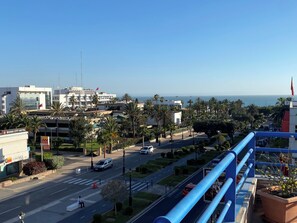 A cityscape with a view of the sea, palm trees, and a modern building with a flag.