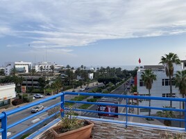Un balcone con vista su una strada cittadina, palme e un cartellone pubblicitario di KFC.