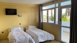 Una habitación con dos camas, un televisor montado en la pared y un ventanal con cortinas.