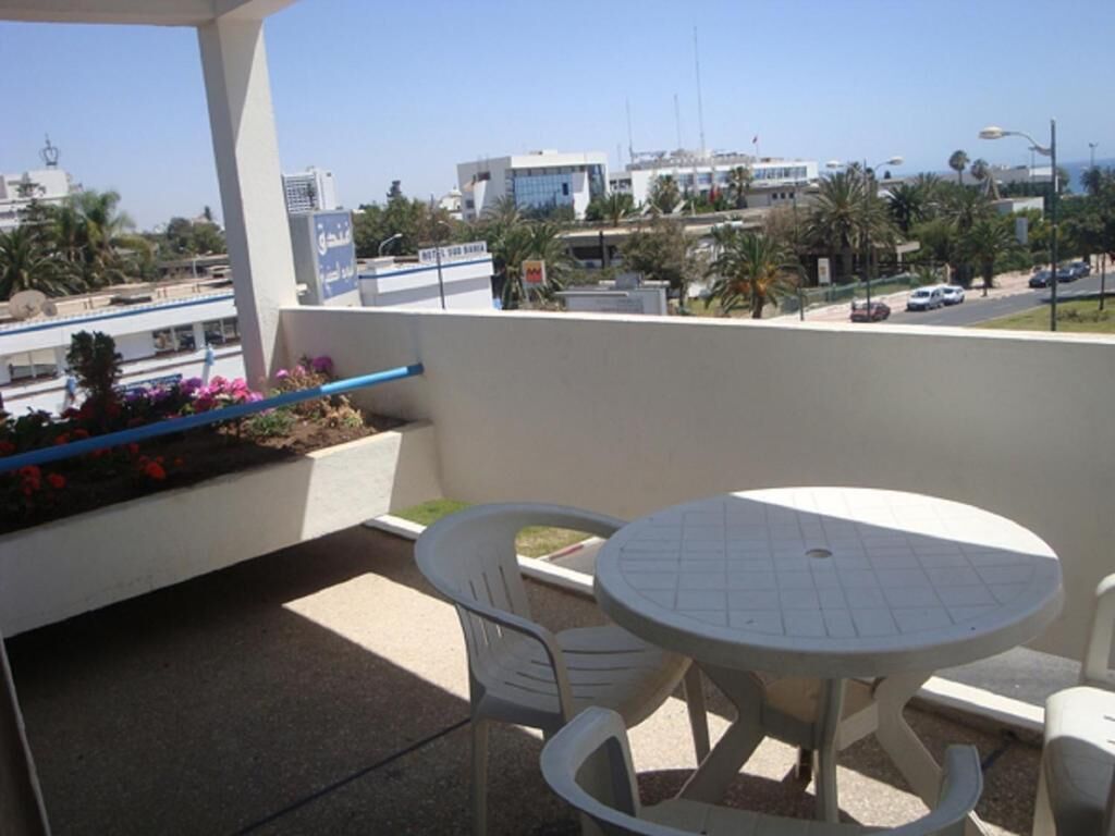 Un balcón con una mesa redonda y dos sillas, con vistas a un paisaje urbano con edificios y palmeras.