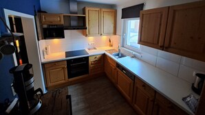 A compact kitchen with wooden cabinets, a built-in oven, and a window providing natural light. - Op een Prachtige Plek in Oostenrijk Staat ons Chalet een Mooi Stekkie (Döllach)