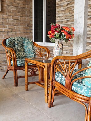 A wicker chair with a patterned cushion and a vase with flowers on a tiled floor.