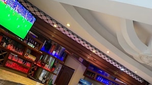 Zona de bar com balcão, banquetes e uma televisão mostrando um jogo esportivo.