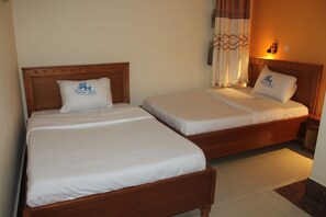 Dos camas individuales con cabeceros de madera y ropa de cama blanca, una mesita de noche y una lámpara fijada a la pared.