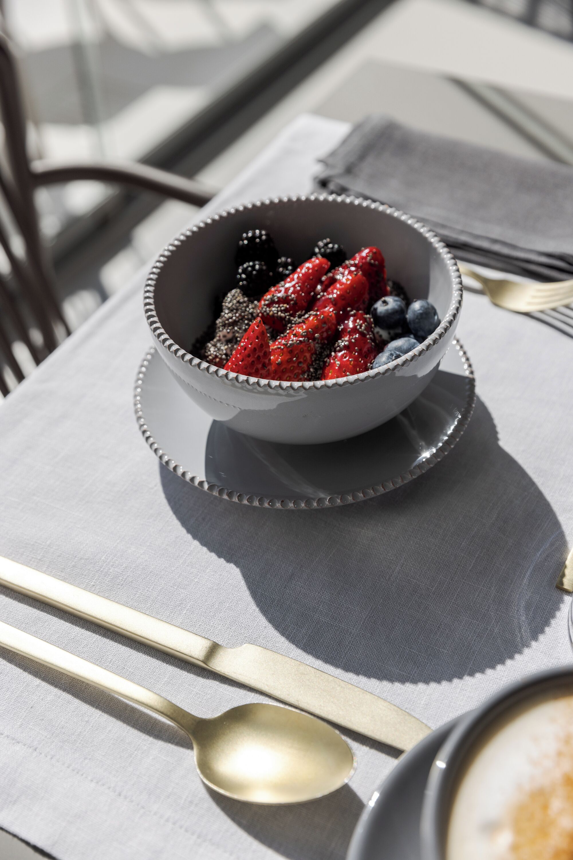 Un bol rempli de fruits rouges variés, posé sur une table, avec une cuillère et une tasse de café.