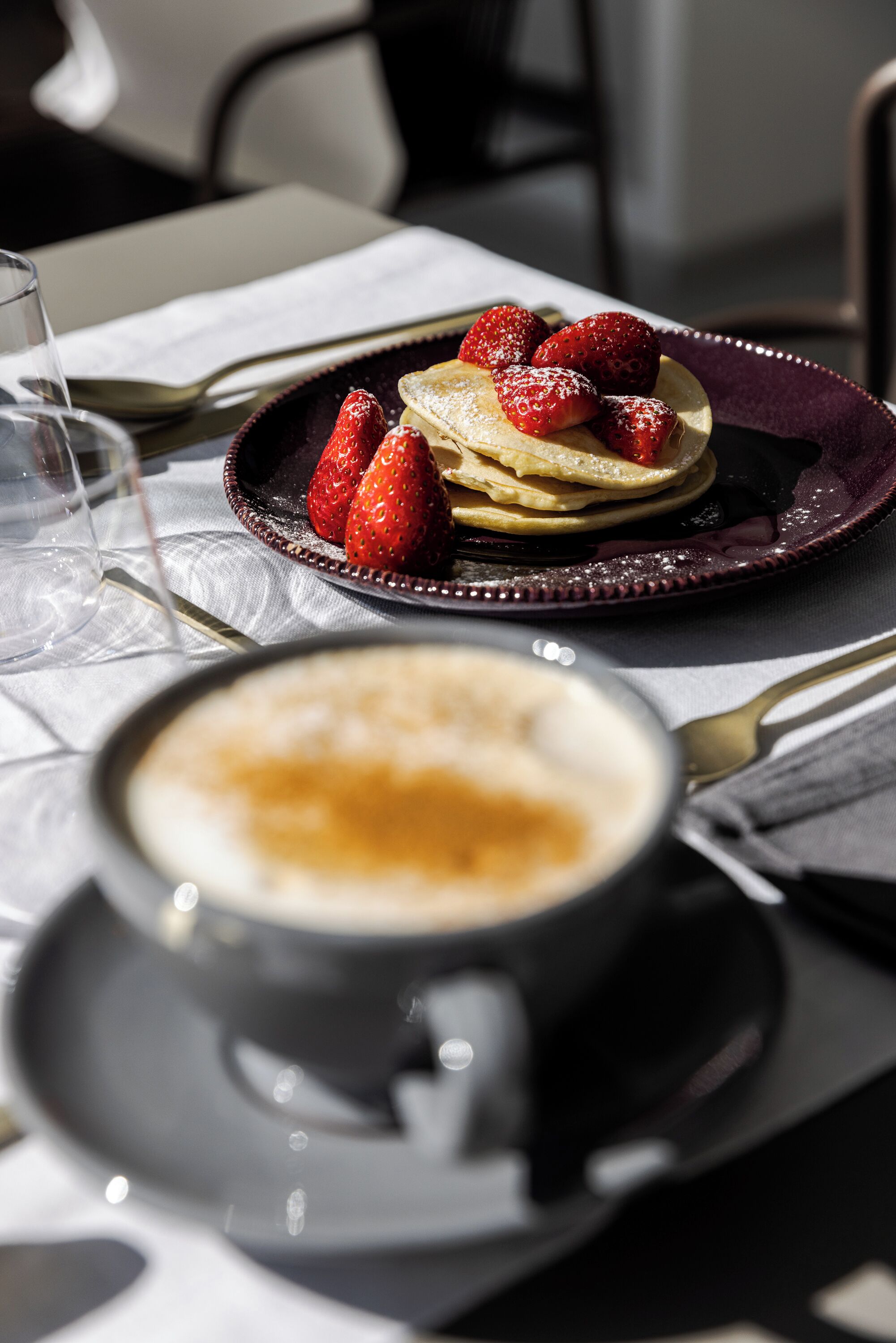 A breakfast setting with pancakes topped with strawberries and a cup of coffee on a table.