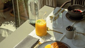 Una mesa de desayuno con un vaso de jugo de naranja, un sándwich y un tazón de fruta.