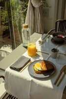 Una mesa de desayuno con un vaso de jugo de naranja, un sándwich y un tazón de fruta.
