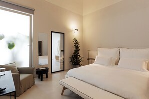 Relax in a serene space with a large bed, bedside table, and chair, surrounded by a potted plant and natural light.
