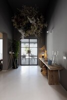 Un interior moderno con un arreglo de plantas colgantes, un banco de madera y una mesa de vidrio con una lámpara.