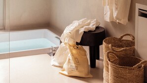 Un baño con bañera, un perchero con una toalla blanca, un bolso y una cesta de mimbre.