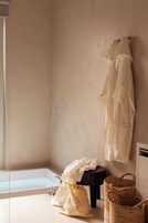 Un baño con una bañera, un perchero con una toalla blanca, una bolsa blanca y una cesta tejida.