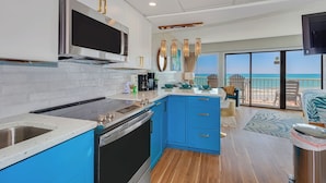A modern kitchen with blue cabinets, stainless steel appliances, and a large window overlooking a beach. - Huge 25 foot circle balcony/MODERN COASTAL/Best view in Myrtle Beach (Myrtle Beach)