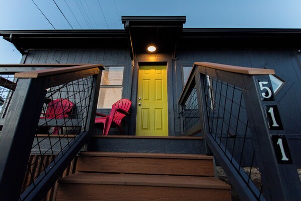 A house with a yellow door, a staircase with wooden steps, and a red chair outside.