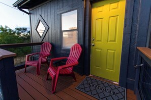 A wooden deck with two red Adirondack chairs and a green door.