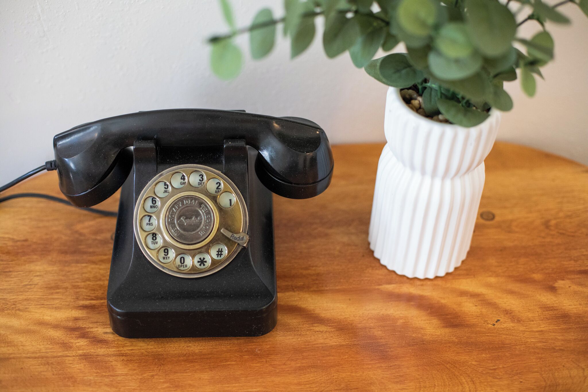 Un telefono da tavolo vintage nero con tastiera rotativa su un piano di legno.