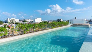 A clear blue pool with a view of a cityscape and a row of palm trees. - Anah 410 2 Bedroom Condo by RedAwning (Playa del Carmen)