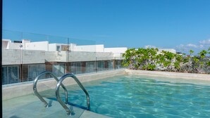 A rooftop swimming pool with clear blue water, metal pool ladder, and a view of buildings and greenery. - Anah 410 2 Bedroom Condo by RedAwning (Playa del Carmen)