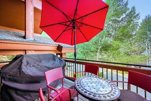 Un espace extérieur abrité, avec une table en mosaïque, des chaises en osier et un parasol rouge.