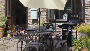 A stone building with a patio area featuring a table and chairs, an umbrella, and a barbecue grill.