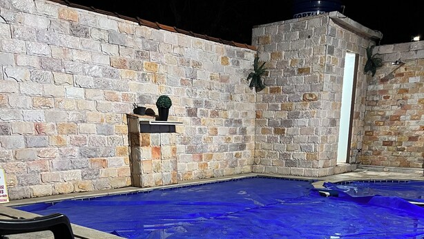 An outdoor swimming pool with stone walls and a chair.