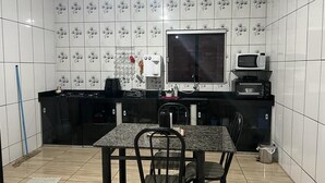 A compact kitchen with white tiled walls, a black countertop, a large window, and a dining area with a table and chairs.