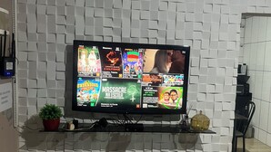 A flat-screen TV mounted on a white brick-patterned wall, displaying various TV channels.