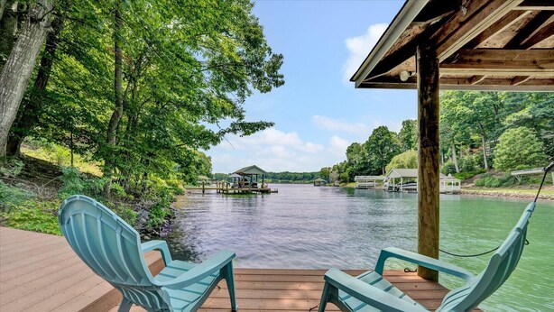 A wooden deck with two turquoise chairs facing a calm lake, surrounded by lush greenery and a gazebo in the distance. - 🌊 Lakefront Getaway with 🏖 Saltwater Pool, 🎣 Dock, 🛏 Linens Included (Moneta)