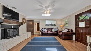 A cozy living room with a fireplace, leather sofas, a blue rug, and a sign reading "Eastlake Cottage". - 🌊 Lakefront Getaway with 🏖 Saltwater Pool, 🎣 Dock, 🛏 Linens Included (Moneta)