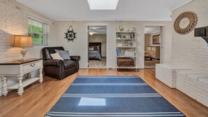 A spacious living room with a large blue rug, a leather sofa, a white brick wall, and a bookshelf. - 🌊 Lakefront Getaway with 🏖 Saltwater Pool, 🎣 Dock, 🛏 Linens Included (Moneta)