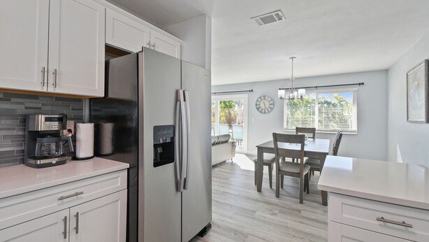 Una cocina moderna con armarios blancos, electrodomésticos de acero inoxidable y un comedor con mesa y sillas.