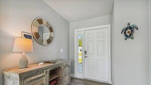 Un pasillo con una consola de madera, un espejo montado en la pared, una puerta blanca y una decoración de tortuga en la pared.
