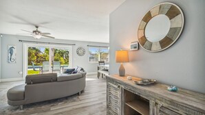 Una sala de estar moderna con un sofá seccional gris, una mesa de centro de madera y un espejo redondo en la pared.