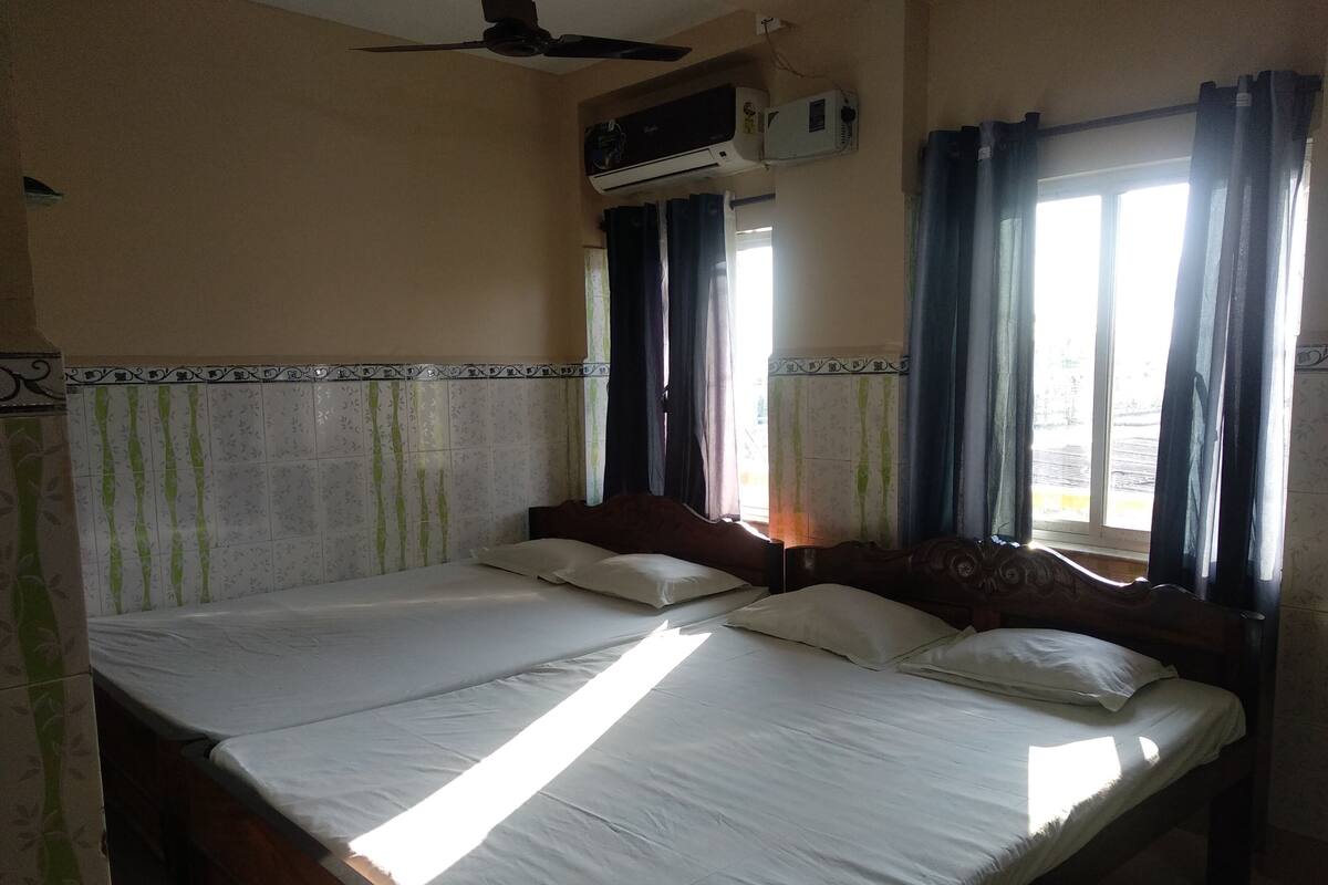 Habitación de hotel con dos camas, ventilador de techo, aire acondicionado y ventanas con cortinas.