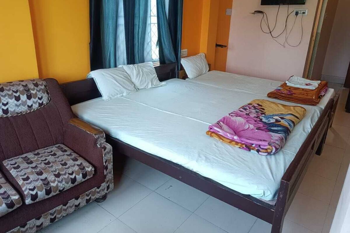 Una habitación de hotel con cama, sofá, televisión instalada en la pared y ventana con cortinas.