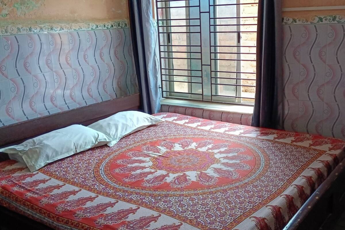Una habitación con una cama, una ventana con barrotes, paredes con diseño y una cortina.