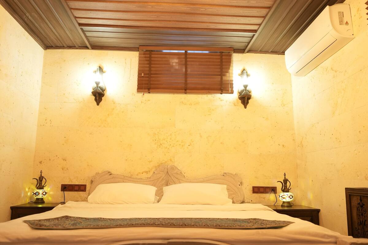 A bedroom with a wooden ceiling, a bed with ornate headboard, two wall sconces, and a ceiling light fixture.