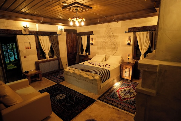 A bedroom with a large bed, a wooden headboard, a nightstand, a bedside table, and a wall-mounted lamp. - Cevizli Konak (Nevsehir)