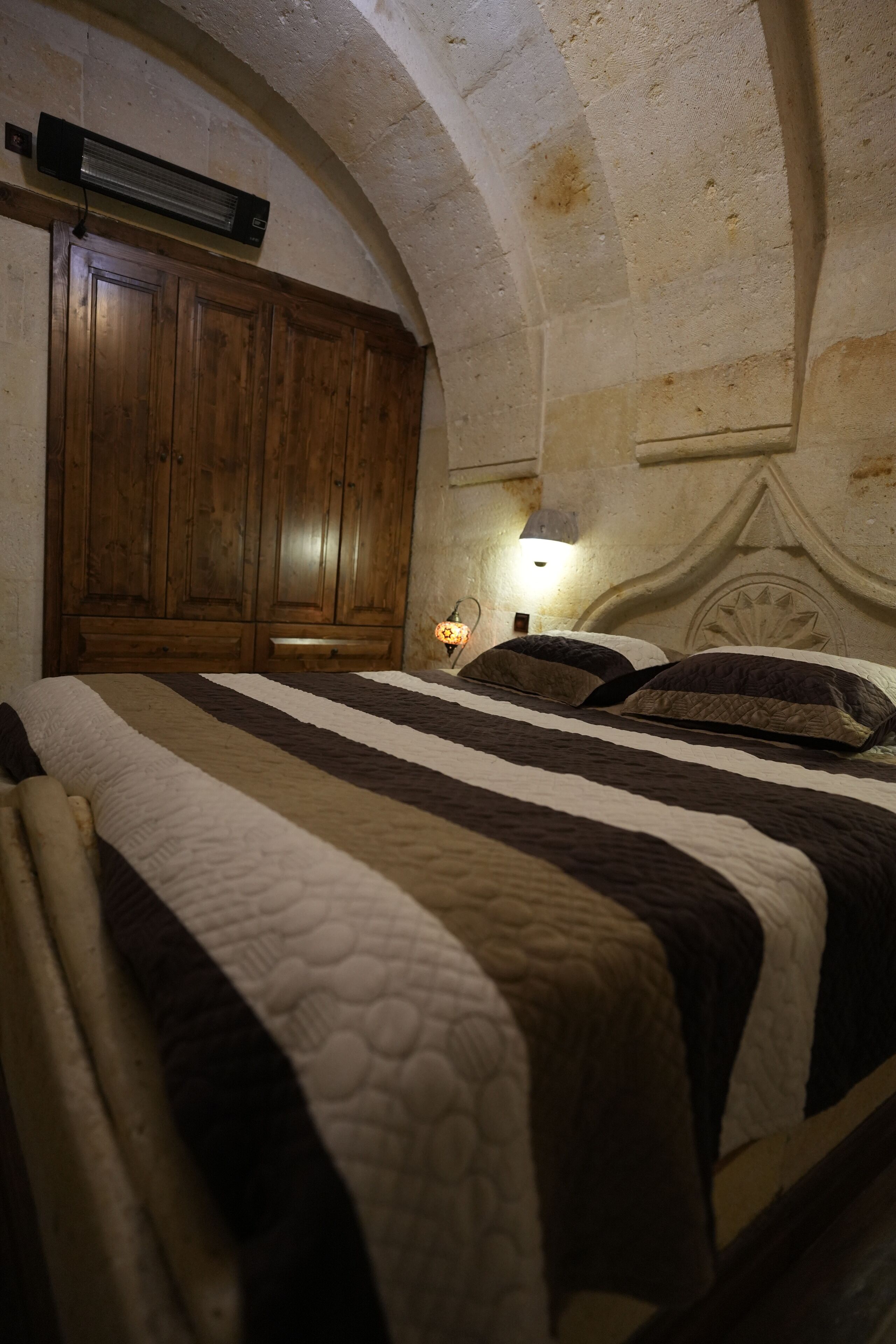 A bedroom with a large bed, wooden wardrobe, and a wall-mounted heater.