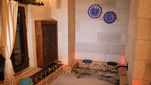 A hot tub with a wooden frame and a stone surround, a wooden cabinet, and two blue decorative plates on the wall. - Cevizli Konak (Nevsehir)
