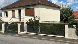 Ein zweistöckiges Haus mit einem Ziegeldach, einem eingezäunten Auffahrt und einer Steinmauer.