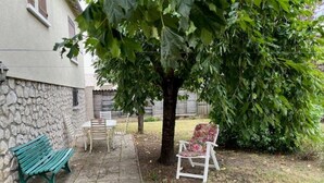 Eine Steinsäule, eine grüne Bank, ein weißer Stuhl und ein Tisch in einem Garten.